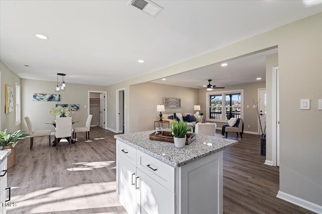 kitchen featuring dark hardwood / wood-style floors, light stone countertops, pendant lighting, white cabinets, and ceiling fan