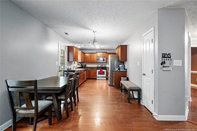 kitchen featuring hanging light fixtures, appliances with stainless steel finishes, a textured ceiling, hardwood / wood-style flooring, and sink