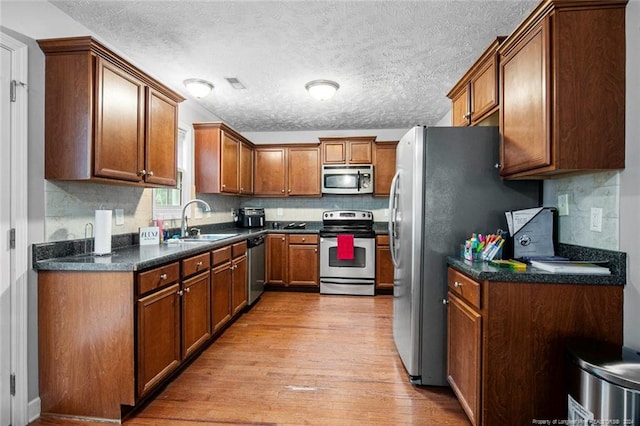 kitchen featuring a textured ceiling, light hardwood / wood-style flooring, dark stone countertops, sink, and stainless steel appliances