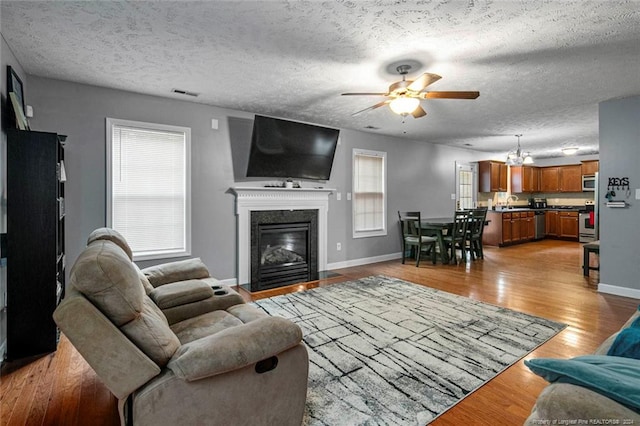 living room with light hardwood / wood-style flooring, a textured ceiling, sink, and ceiling fan with notable chandelier