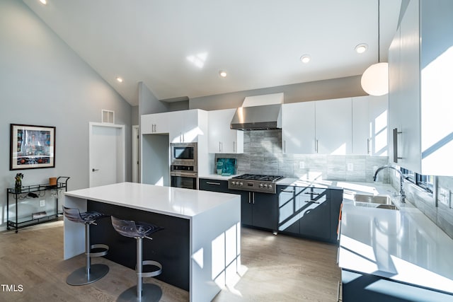 kitchen with a kitchen island, wall chimney range hood, appliances with stainless steel finishes, hanging light fixtures, and white cabinets