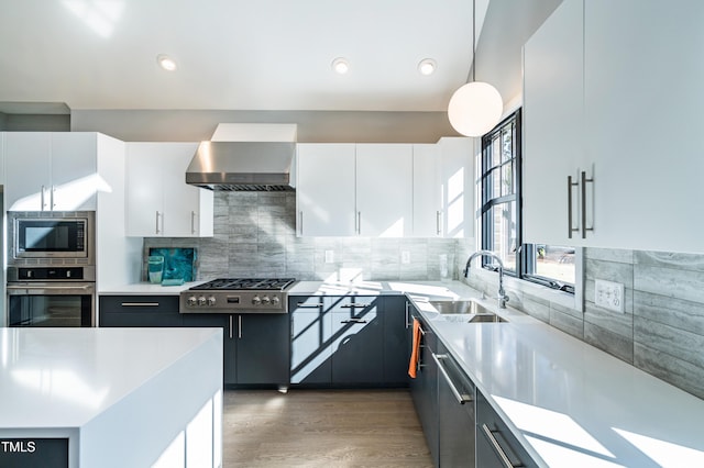 kitchen with stainless steel appliances, sink, white cabinets, wall chimney range hood, and pendant lighting