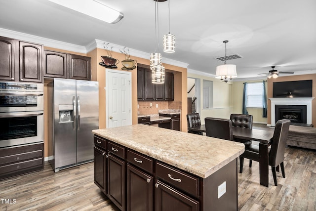 kitchen with appliances with stainless steel finishes, dark brown cabinets, pendant lighting, light hardwood / wood-style flooring, and a kitchen island