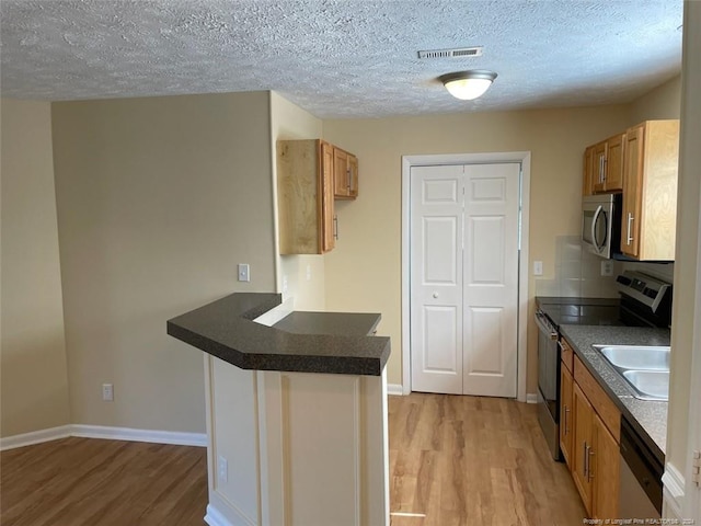 kitchen with appliances with stainless steel finishes, sink, light wood-type flooring, a textured ceiling, and kitchen peninsula