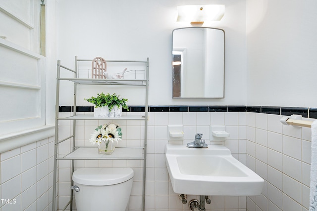 bathroom featuring toilet, tile walls, and sink