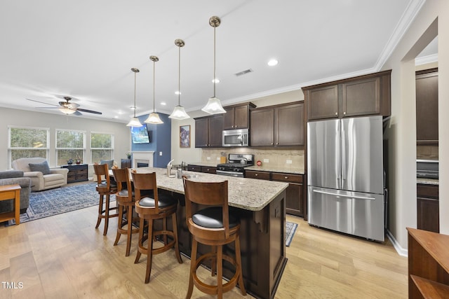 kitchen with a breakfast bar area, hanging light fixtures, an island with sink, stainless steel appliances, and light stone countertops