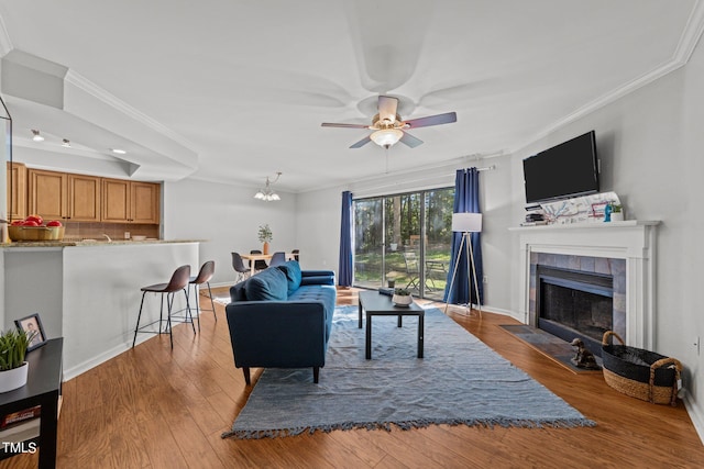 living room with a tiled fireplace, ornamental molding, light hardwood / wood-style flooring, and ceiling fan with notable chandelier