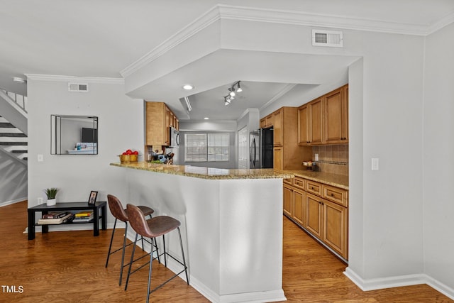 kitchen with black fridge, a kitchen breakfast bar, kitchen peninsula, ornamental molding, and light hardwood / wood-style floors