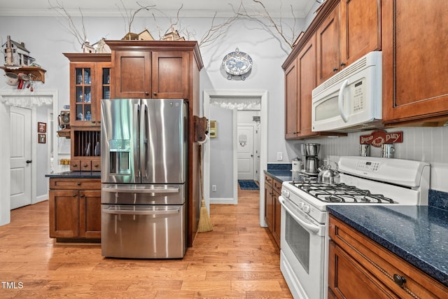 kitchen featuring ornamental molding, light hardwood / wood-style flooring, white appliances, and dark stone counters