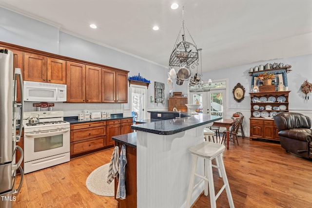 kitchen with a center island with sink, a kitchen breakfast bar, ornamental molding, light hardwood / wood-style floors, and white appliances