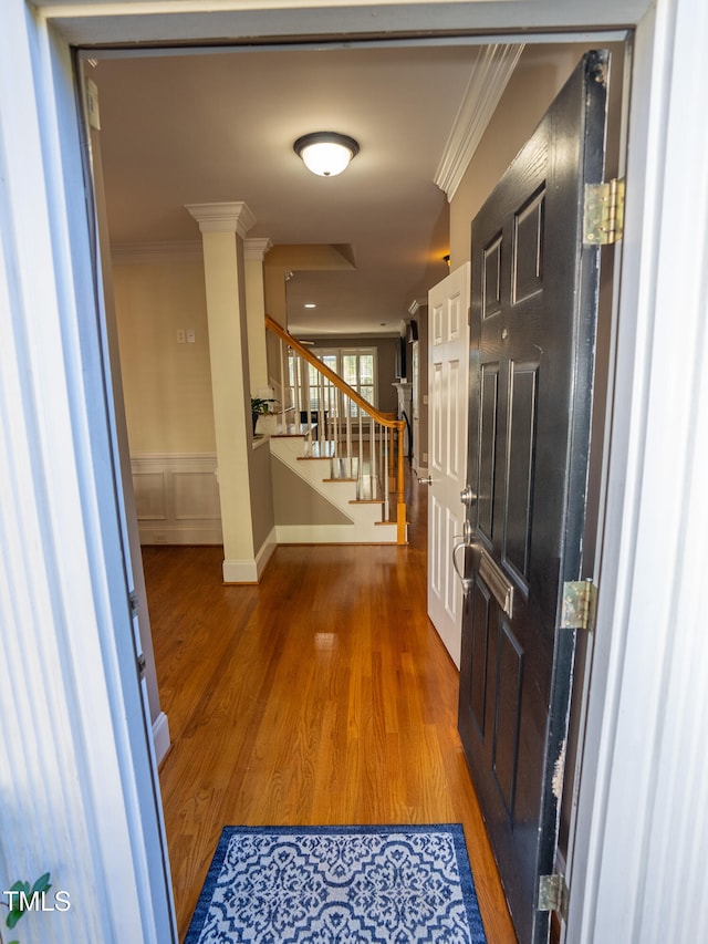 corridor with wood-type flooring, ornate columns, and crown molding