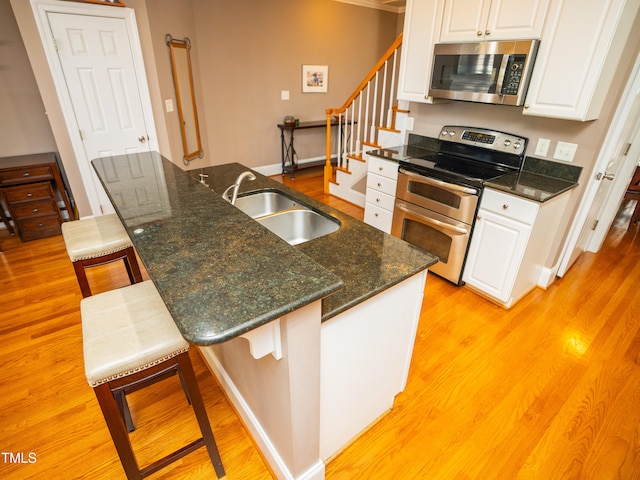 kitchen featuring white cabinets, sink, a kitchen breakfast bar, light wood-type flooring, and appliances with stainless steel finishes