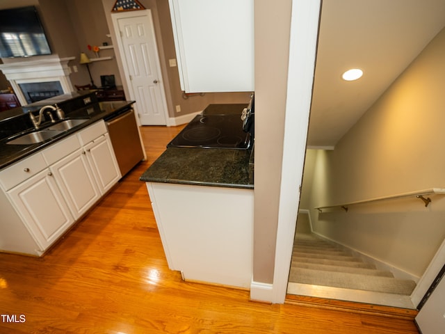 kitchen featuring white cabinetry, light wood-type flooring, sink, black range oven, and dishwasher