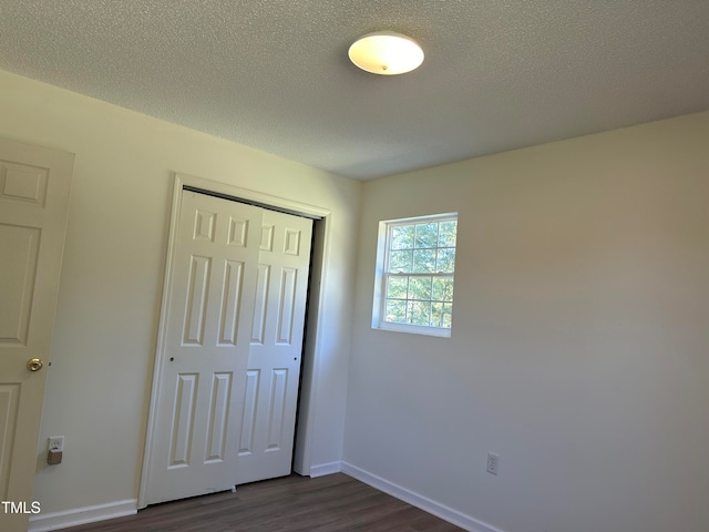 unfurnished bedroom featuring a textured ceiling, dark hardwood / wood-style floors, and a closet