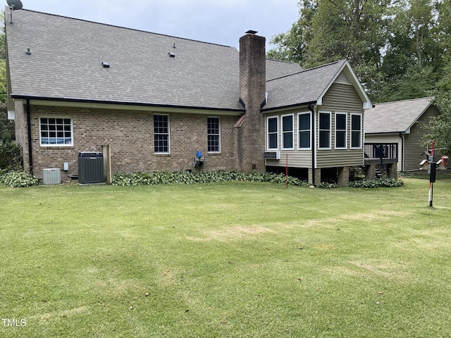 rear view of house featuring central air condition unit and a lawn