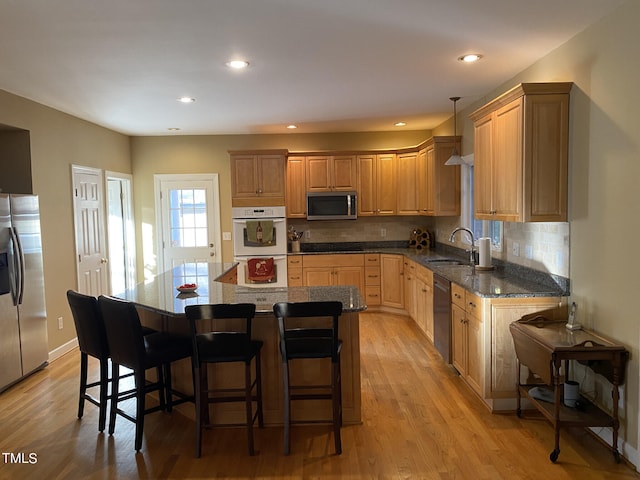 kitchen with hanging light fixtures, a breakfast bar area, appliances with stainless steel finishes, light hardwood / wood-style flooring, and sink