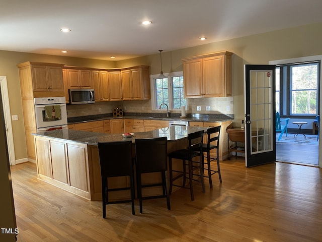 kitchen featuring appliances with stainless steel finishes, a kitchen island, hanging light fixtures, light hardwood / wood-style floors, and dark stone counters