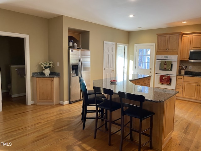 kitchen featuring a spacious island, dark stone counters, a kitchen bar, light wood-type flooring, and appliances with stainless steel finishes