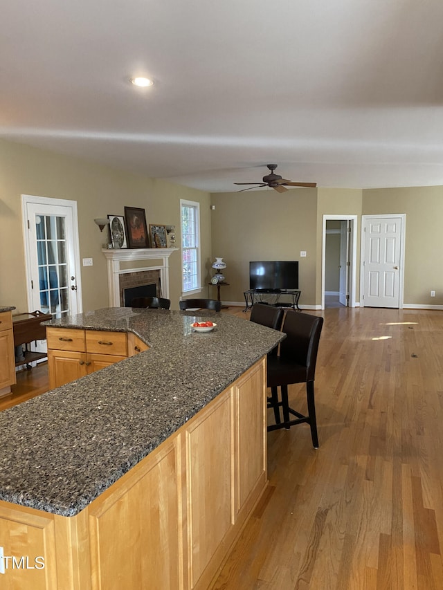 kitchen with dark stone countertops, light hardwood / wood-style floors, light brown cabinets, and ceiling fan