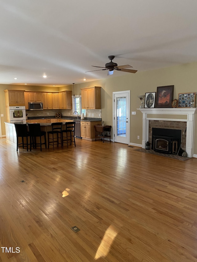 living room featuring sink, wood-type flooring, a tile fireplace, and ceiling fan