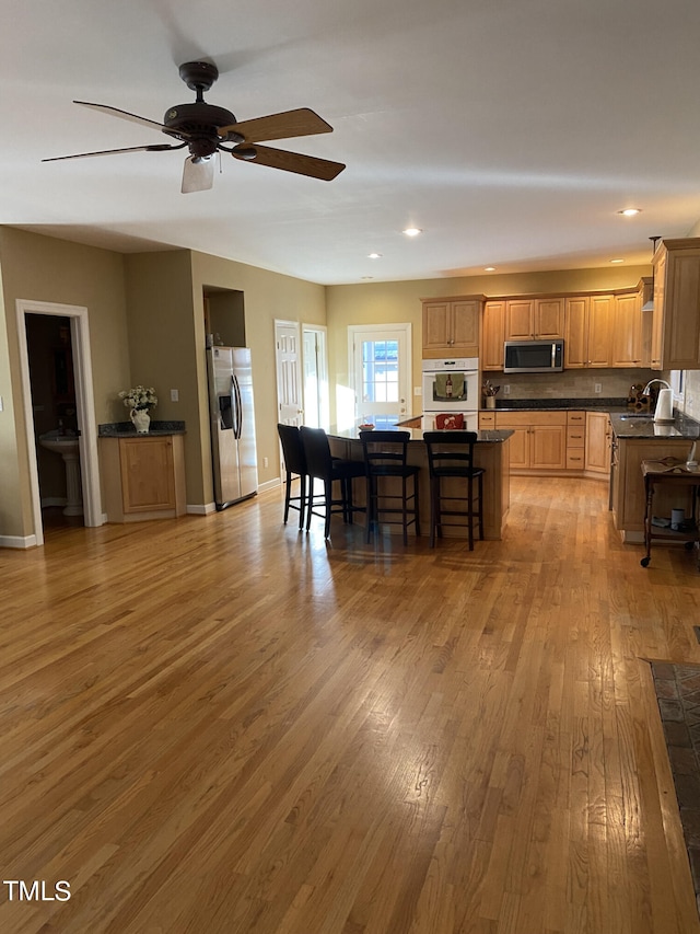 kitchen featuring a kitchen bar, a center island, ceiling fan, stainless steel appliances, and light hardwood / wood-style flooring