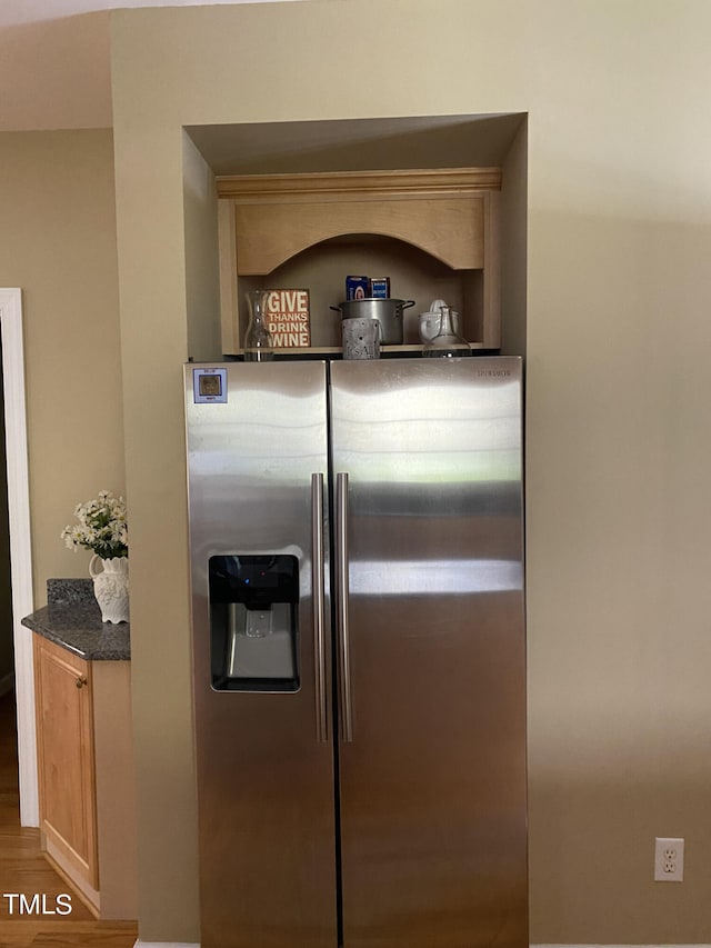 details with light brown cabinetry, dark stone counters, hardwood / wood-style floors, and stainless steel fridge