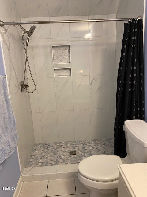 bathroom with vanity, walk in shower, toilet, and tile patterned flooring