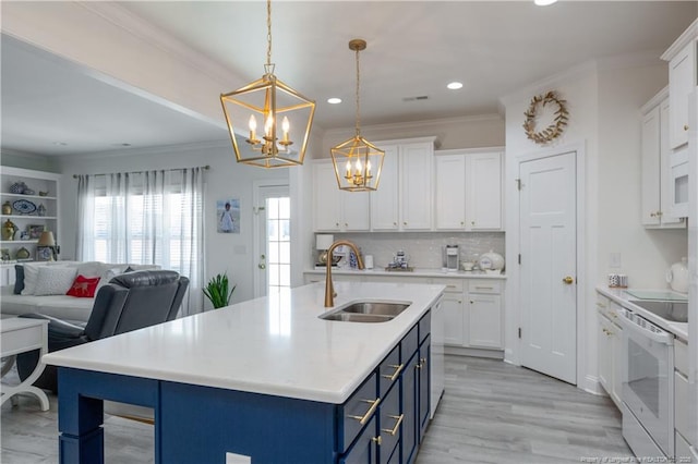 kitchen with white electric range, blue cabinets, sink, hanging light fixtures, and white cabinetry