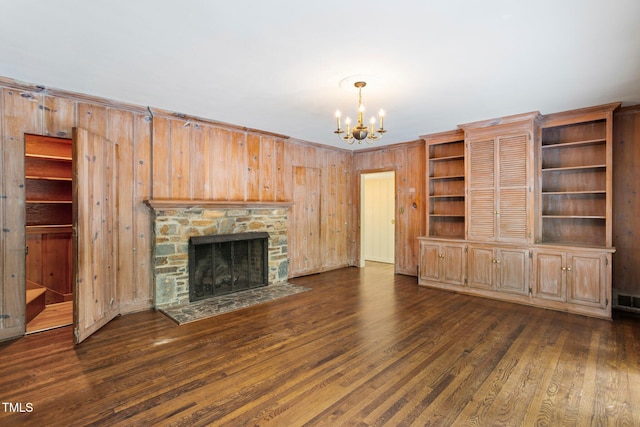 unfurnished living room with an inviting chandelier, wood walls, a fireplace, and dark hardwood / wood-style flooring