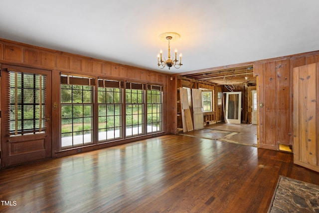 unfurnished room featuring a notable chandelier, a healthy amount of sunlight, dark hardwood / wood-style flooring, and wooden walls