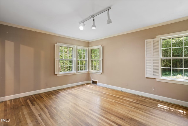 empty room with light hardwood / wood-style flooring, ornamental molding, and track lighting