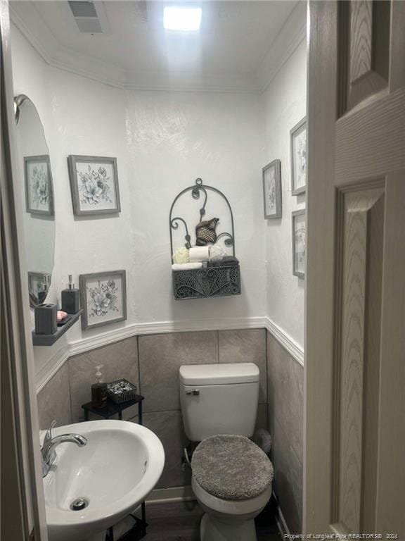 bathroom featuring toilet, tile walls, sink, and ornamental molding