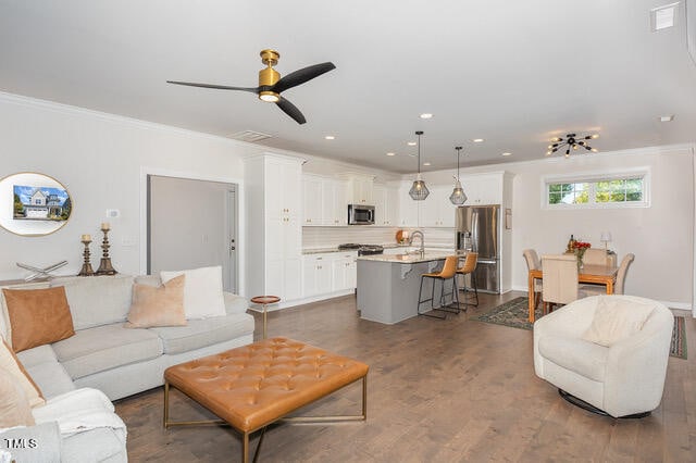 living room featuring dark wood-type flooring, ceiling fan, ornamental molding, and sink