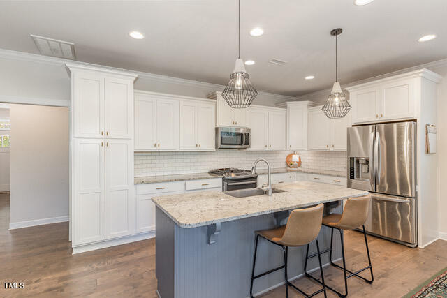 kitchen with white cabinets, an island with sink, dark hardwood / wood-style floors, sink, and stainless steel appliances