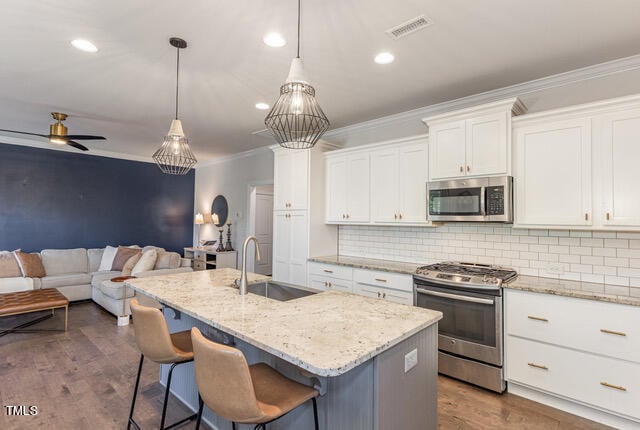 kitchen with dark hardwood / wood-style floors, an island with sink, stainless steel appliances, sink, and white cabinets