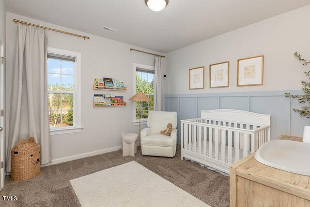 carpeted bedroom featuring multiple windows and a crib