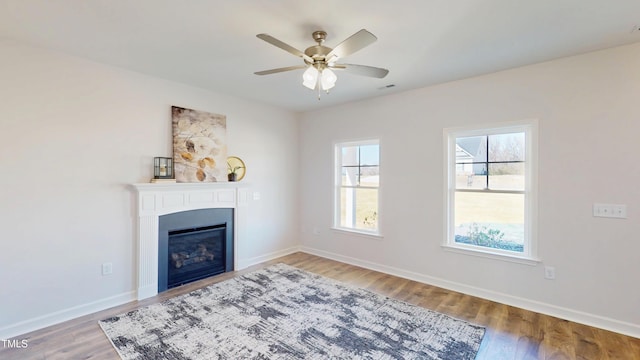 unfurnished living room with a glass covered fireplace, ceiling fan, baseboards, and wood finished floors