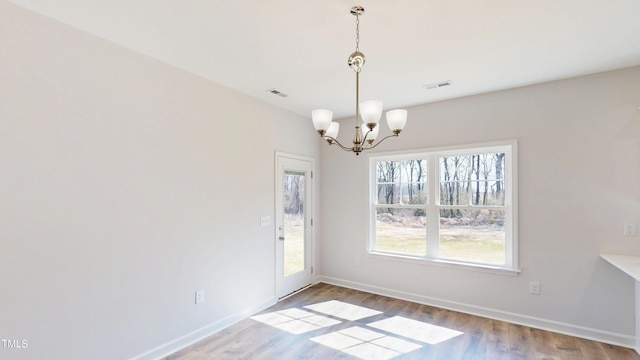 unfurnished dining area featuring a chandelier, wood finished floors, baseboards, and visible vents