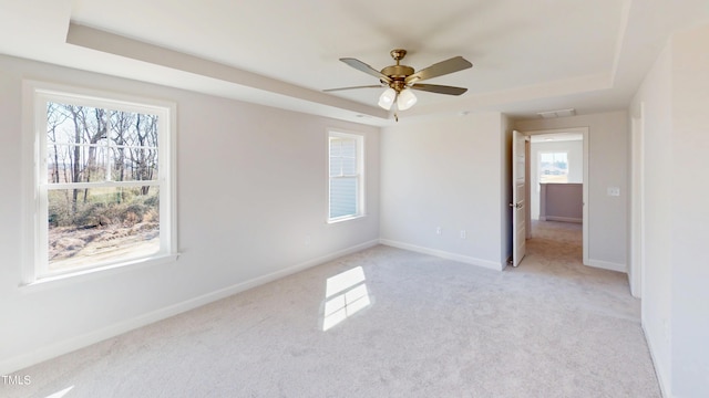 spare room with baseboards, a tray ceiling, light colored carpet, and a ceiling fan