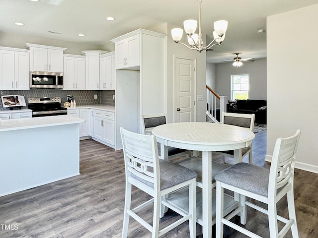 kitchen with white cabinetry, backsplash, dark wood finished floors, stainless steel appliances, and ceiling fan with notable chandelier