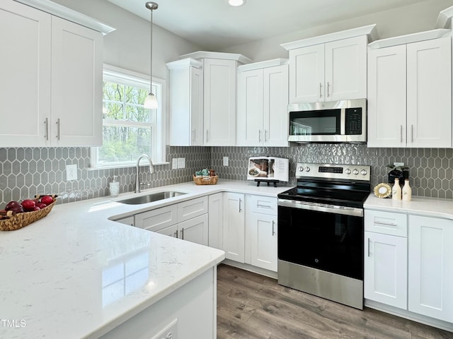 kitchen featuring tasteful backsplash, white cabinets, decorative light fixtures, a sink, and appliances with stainless steel finishes