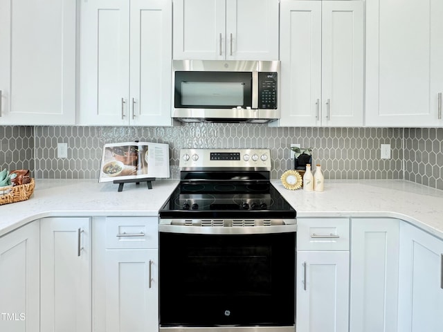 kitchen with white cabinets, appliances with stainless steel finishes, light stone counters, and decorative backsplash