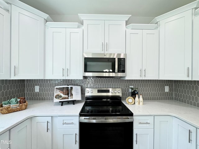 kitchen with stainless steel microwave, white cabinets, light stone countertops, range with electric cooktop, and decorative backsplash