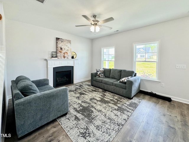 living area with visible vents, baseboards, ceiling fan, a fireplace, and dark wood finished floors