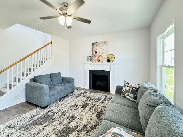 living room featuring ceiling fan, a fireplace, visible vents, stairway, and wood finished floors