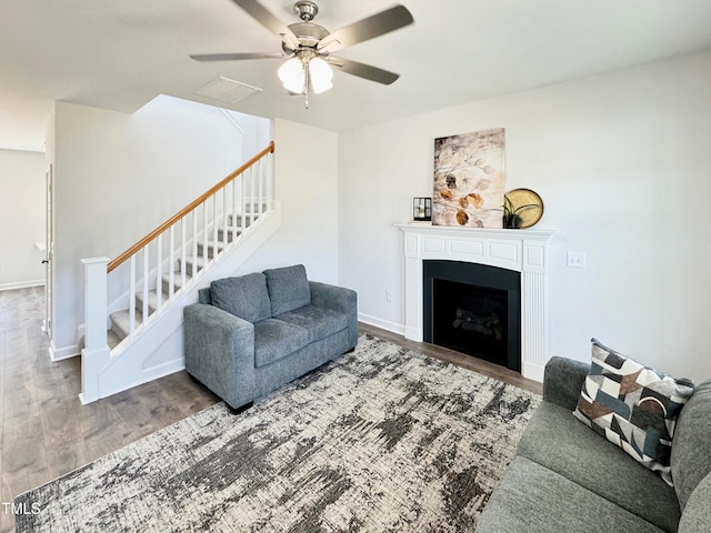living room featuring visible vents, a ceiling fan, a fireplace, wood finished floors, and stairs