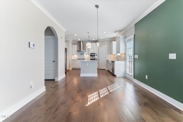 kitchen featuring decorative light fixtures, a kitchen island, crown molding, white cabinets, and wall chimney exhaust hood