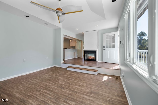 unfurnished living room featuring a multi sided fireplace, a raised ceiling, wood-type flooring, and ceiling fan