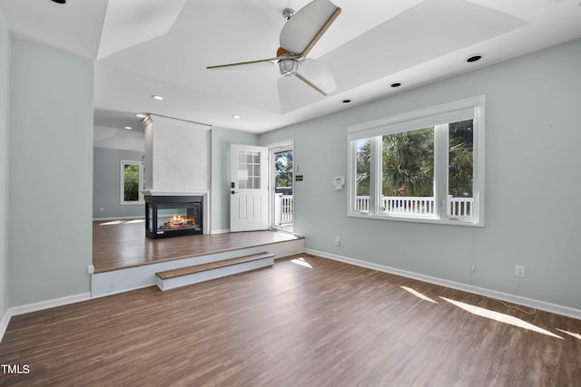 unfurnished living room featuring dark wood-type flooring, a large fireplace, and ceiling fan