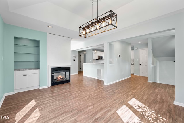 unfurnished living room with a multi sided fireplace, wood-type flooring, and built in shelves